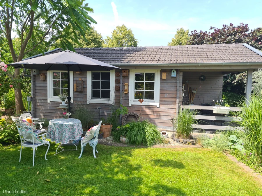 Gartenh&auml;usen mit kleinem Vintagetisch davor. Drei St&uuml;hle mit gem&uuml;tlichen Kissen.